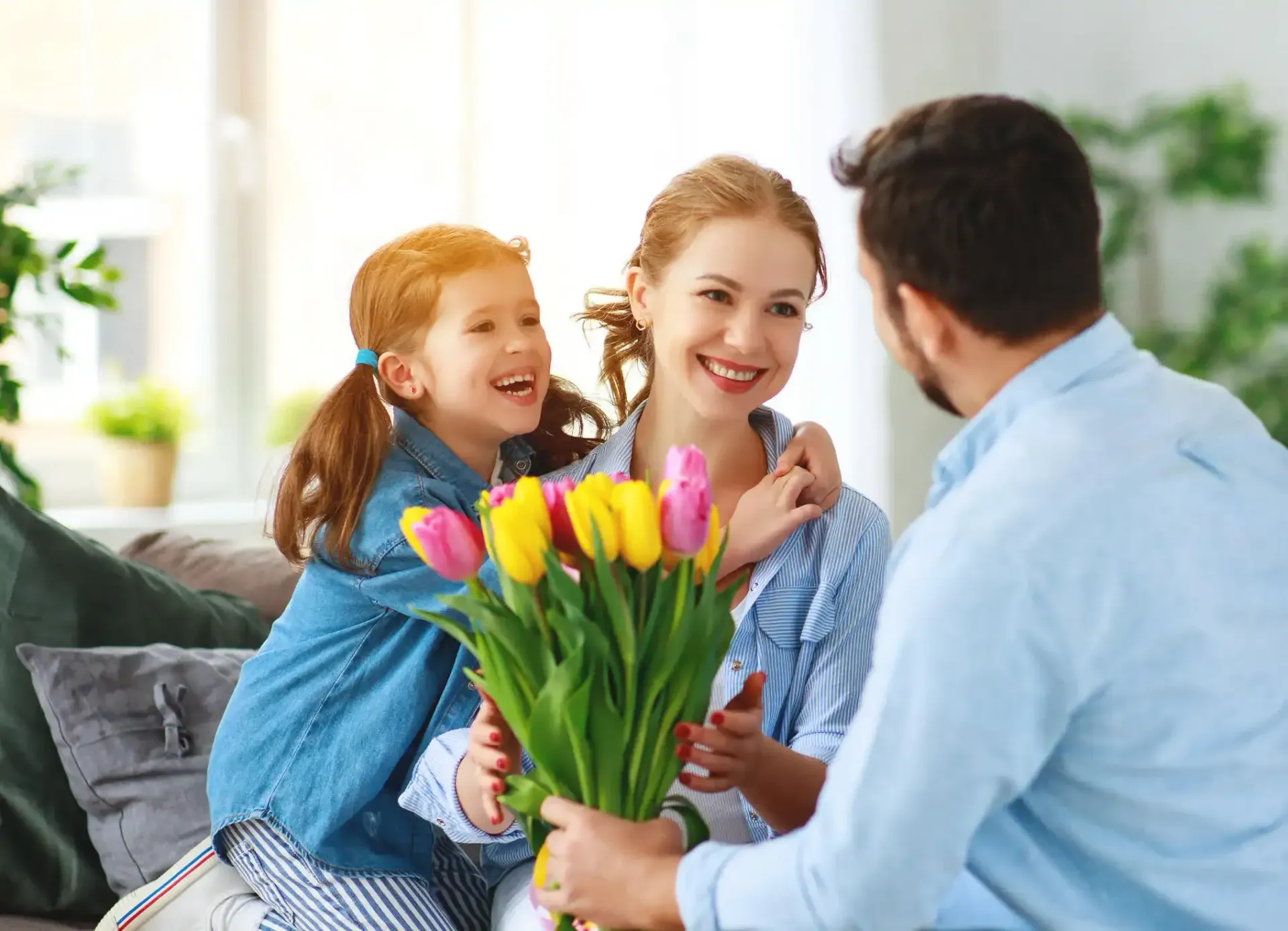 A man and a little girl are sitting on a couch holding a bouquet of flowers.