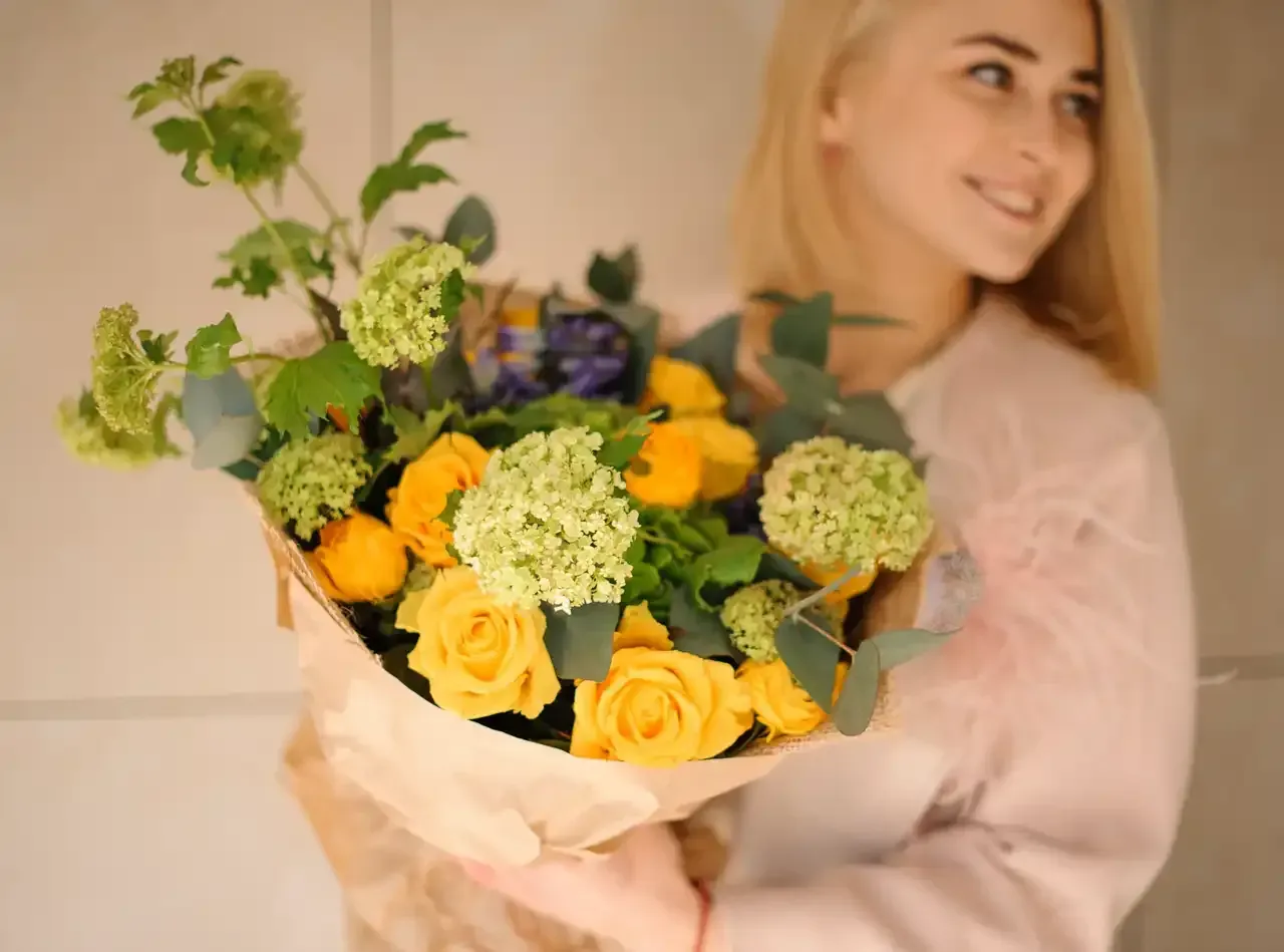 A woman is holding a bouquet of yellow roses and green flowers.
