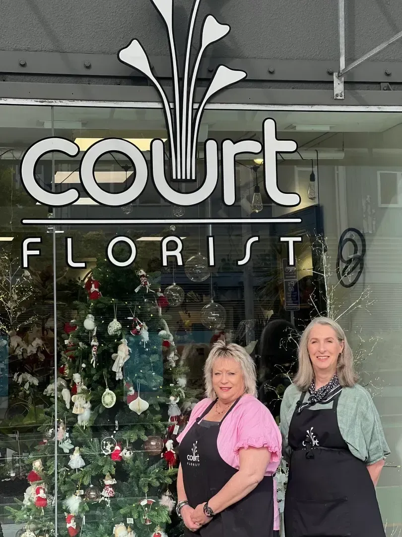 Two women are standing in front of a court florist store.