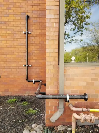 Copper pipes and drain pipes mounted on a brick wall beside a window