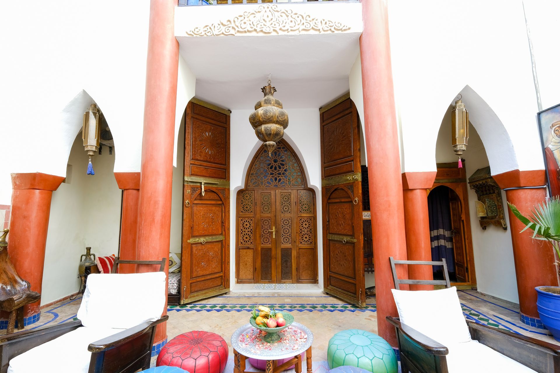 Courtyard with ornate wooden doors, red pillars, seating, and decorative lanterns.
