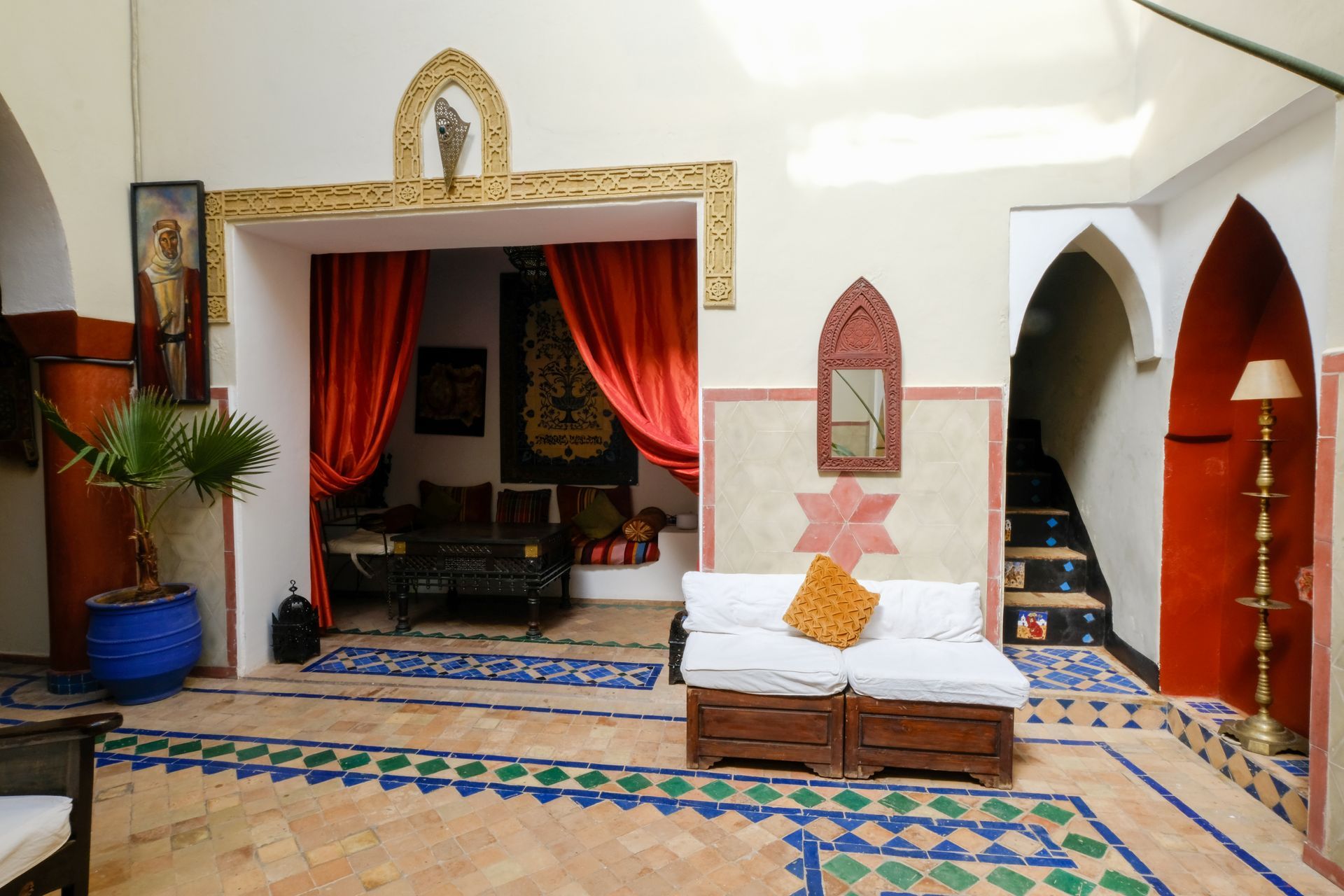 Moroccan-style interior with red accents, archways, tiled floor, and a seating area with red curtains.