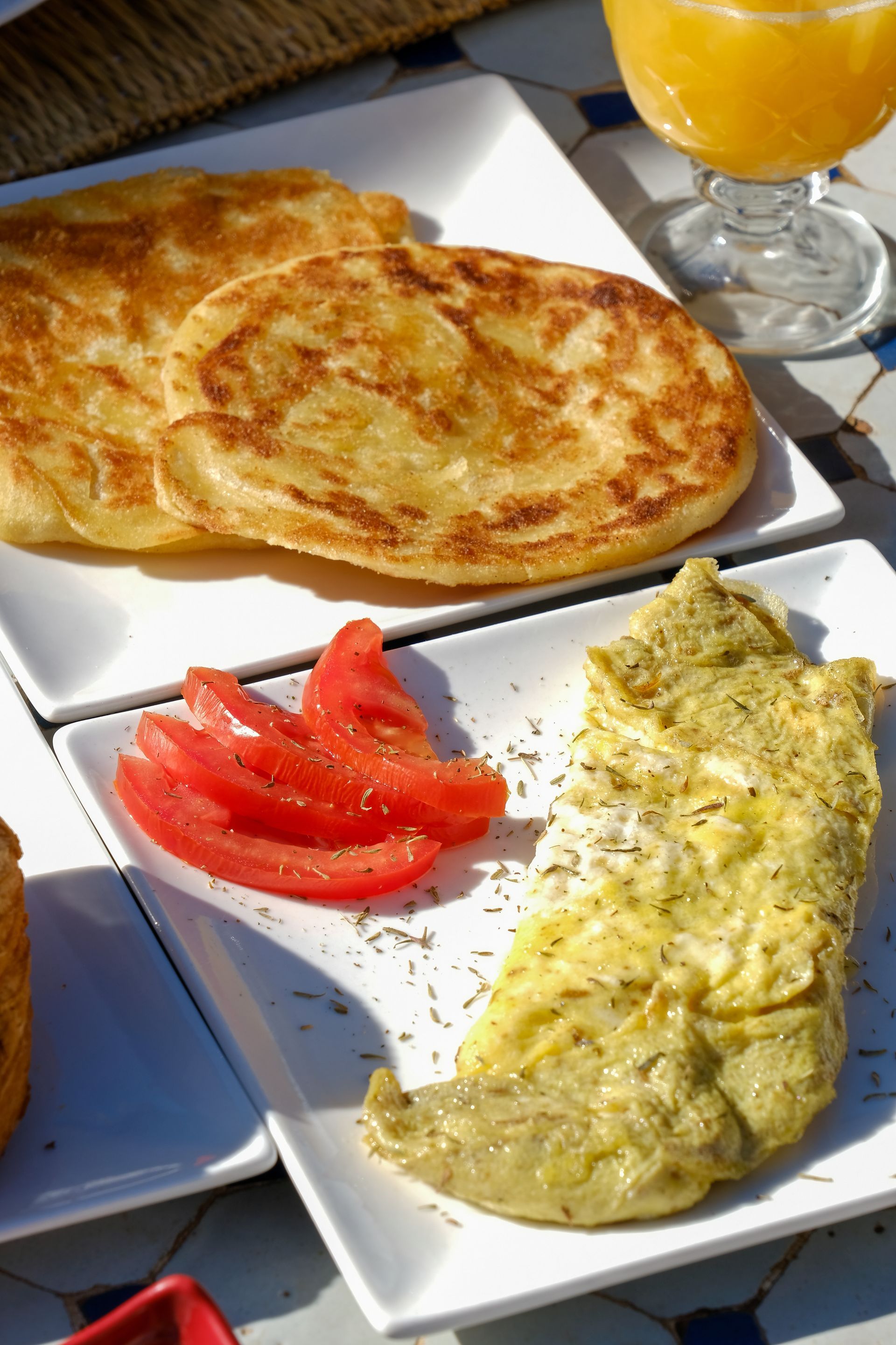 Breakfast: omelet with herbs, sliced tomatoes, flatbread, and orange juice.