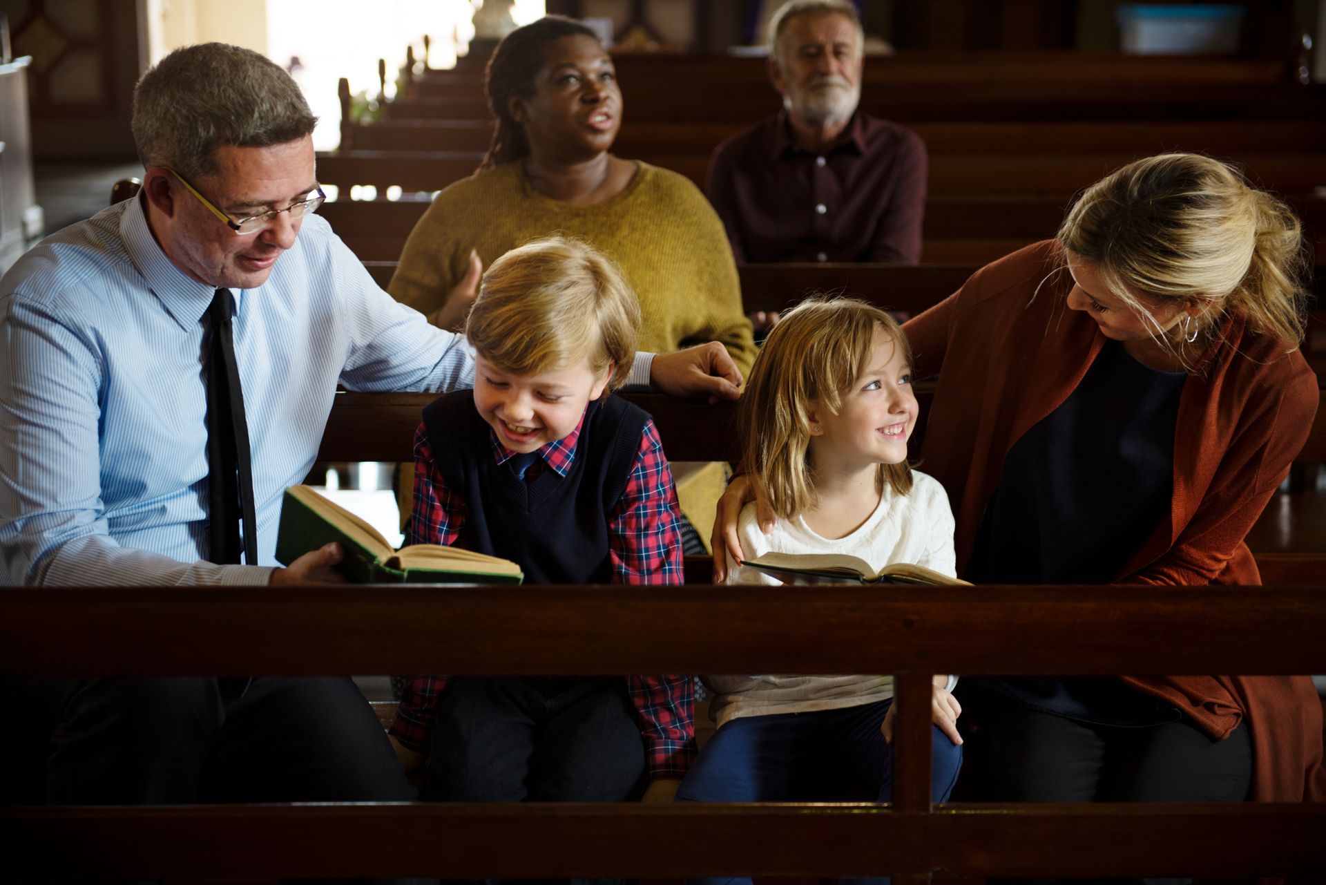 Family in church pew reading books; smiling. Sunlight streams in.