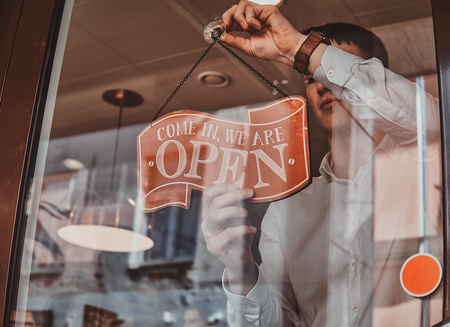 Person hanging an OPEN sign in a shop window