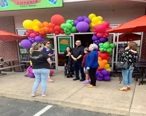 A group of people standing in front of a building with balloons and umbrellas.