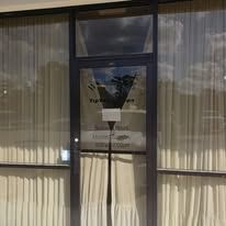 A glass door with a black frame, partially obscured by sheer curtains. Signage on the door reads