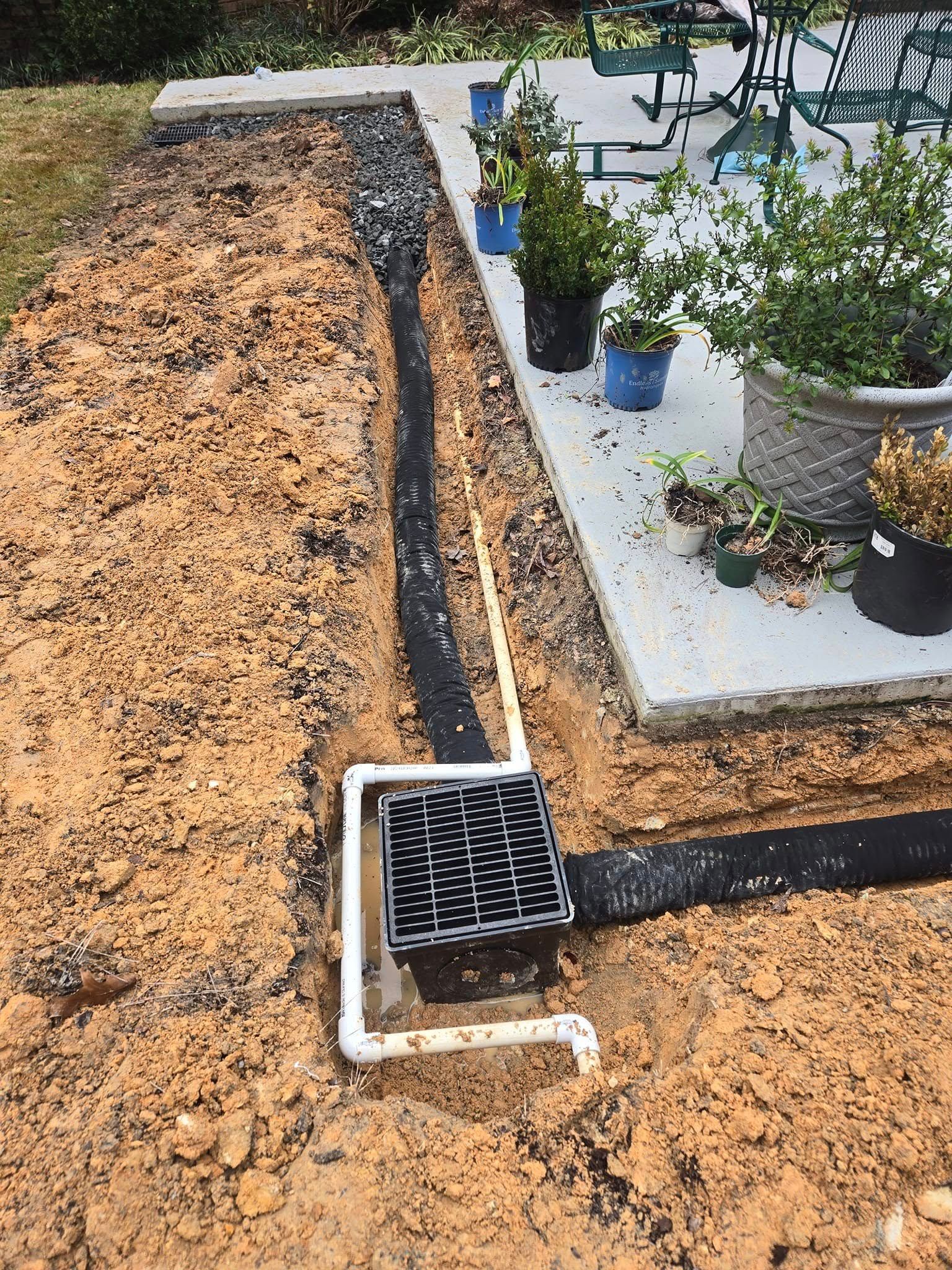 A drain is being installed in the dirt next to a patio.