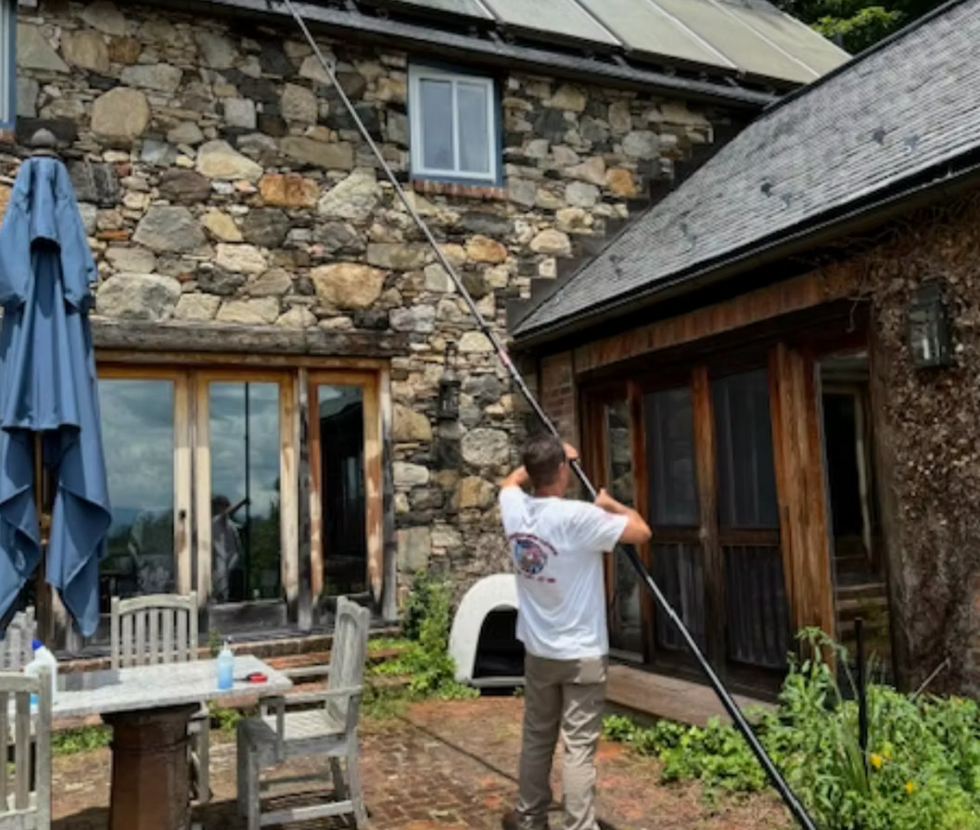 A man is cleaning the roof of a stone house with a hose.