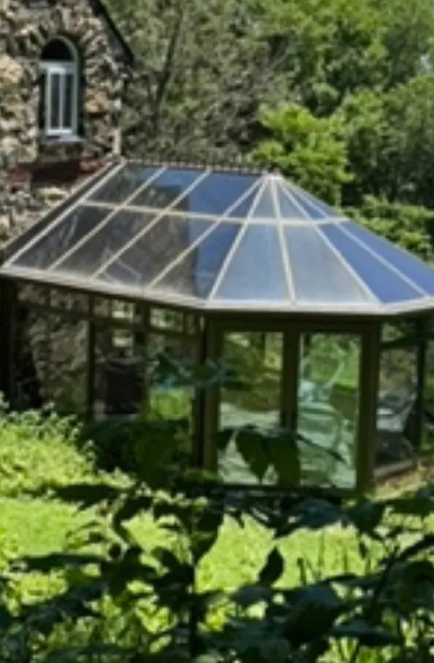 A gazebo with a clear glass roof in front of a stone building