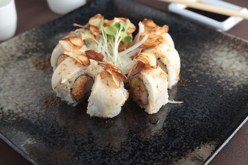 Sushi rolls topped with fried garlic and greens on a black square plate