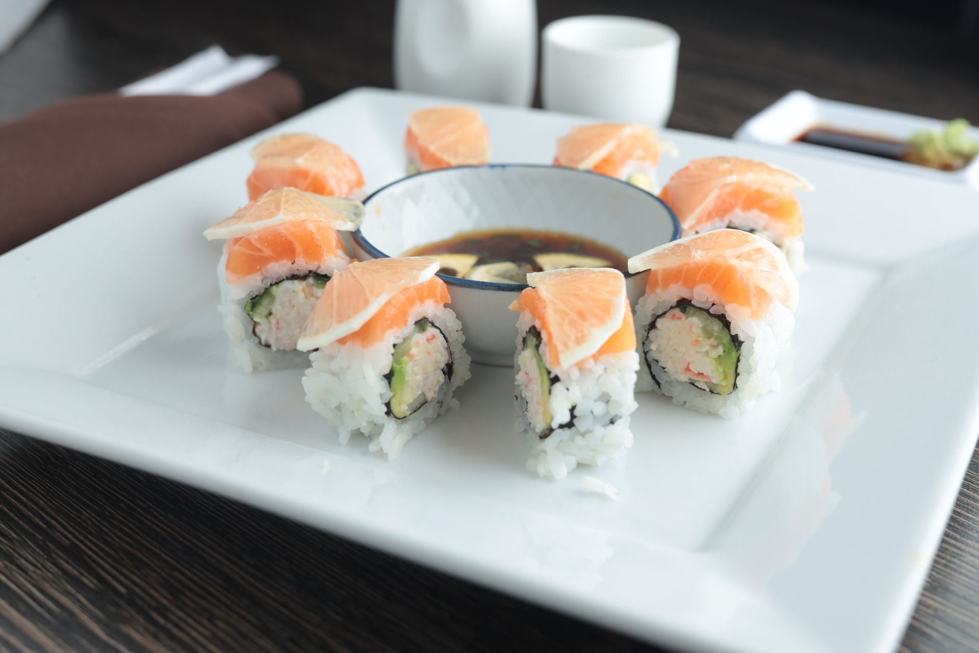 Sushi rolls with salmon arranged on a white square plate around a dipping bowl.