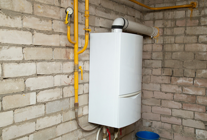 White gas boiler mounted on a brick wall with yellow gas pipes and a vent.