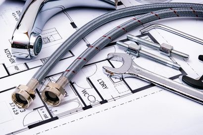 Plumbing tools, faucet, and flexible hoses on top of a blueprint.
