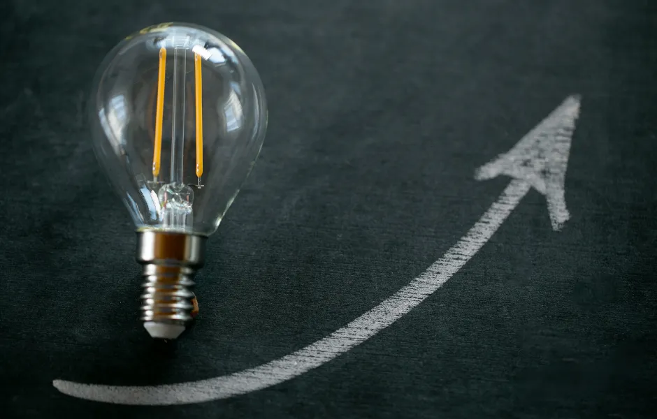 A light bulb is sitting next to an arrow drawn on a blackboard.