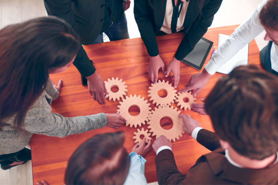 Group of people around a table each putting a hand in the center on gears