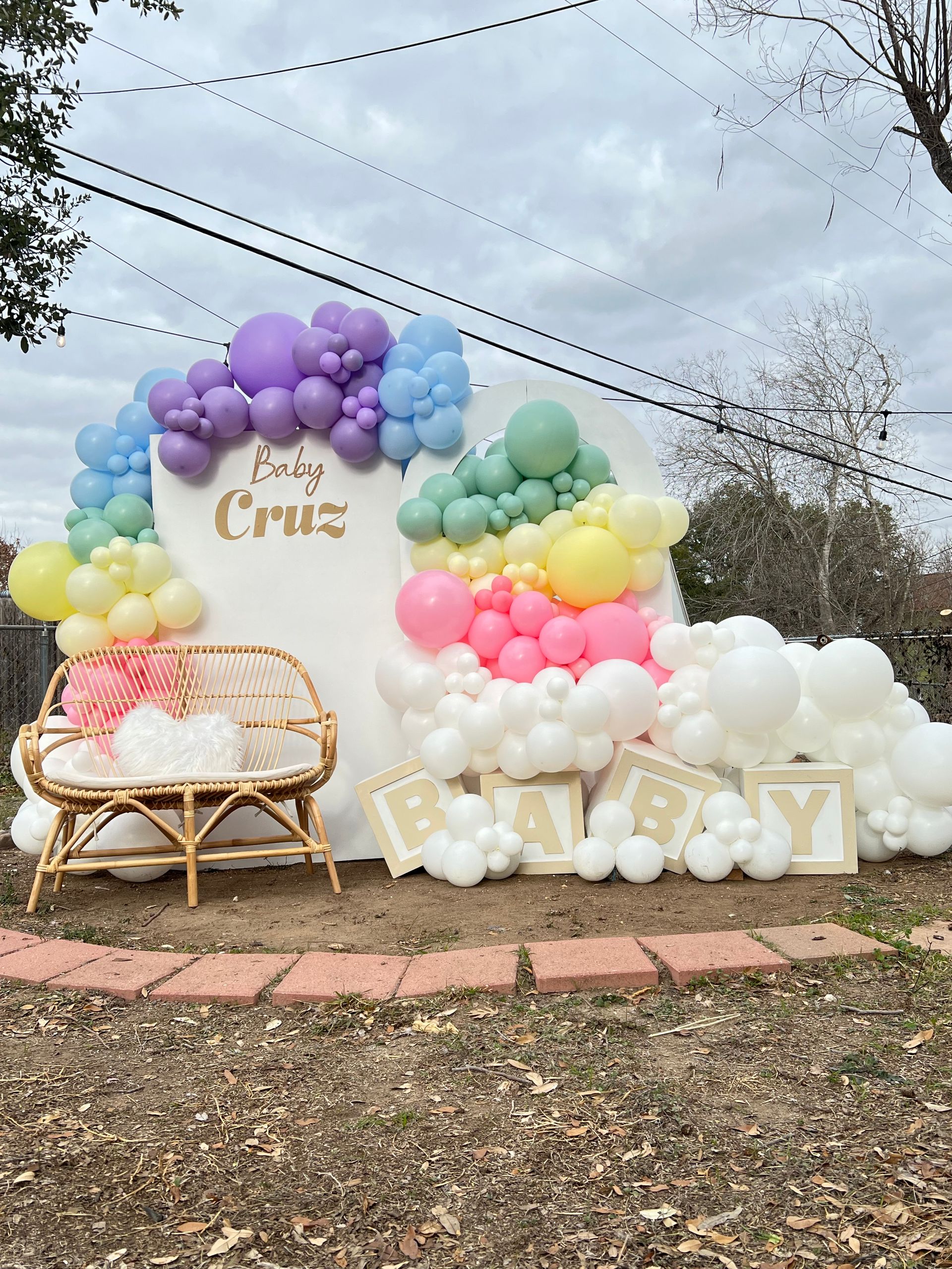 A baby shower backdrop with balloons and a wicker bench.
