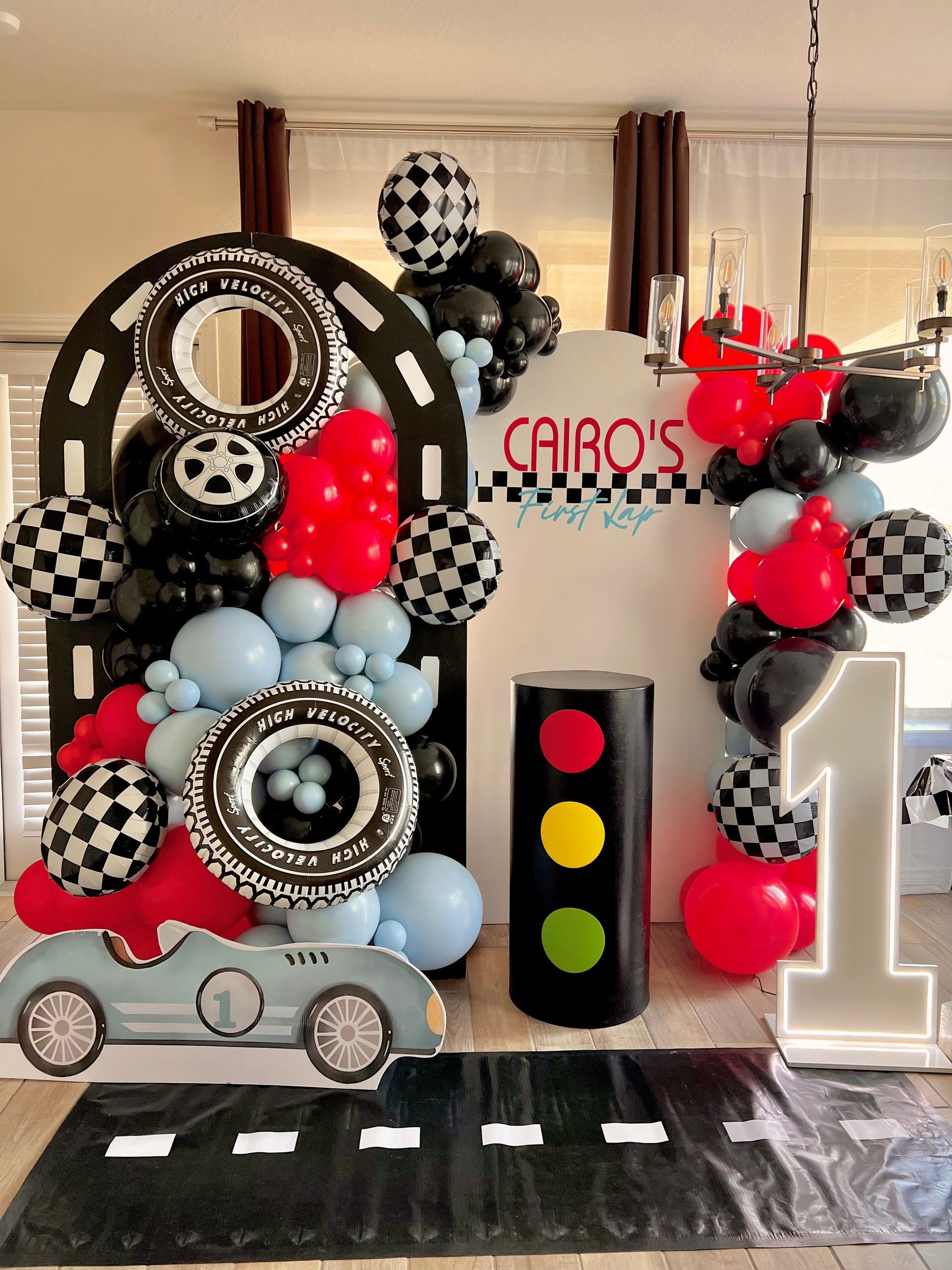 A room decorated with balloons , a car , and a number one.