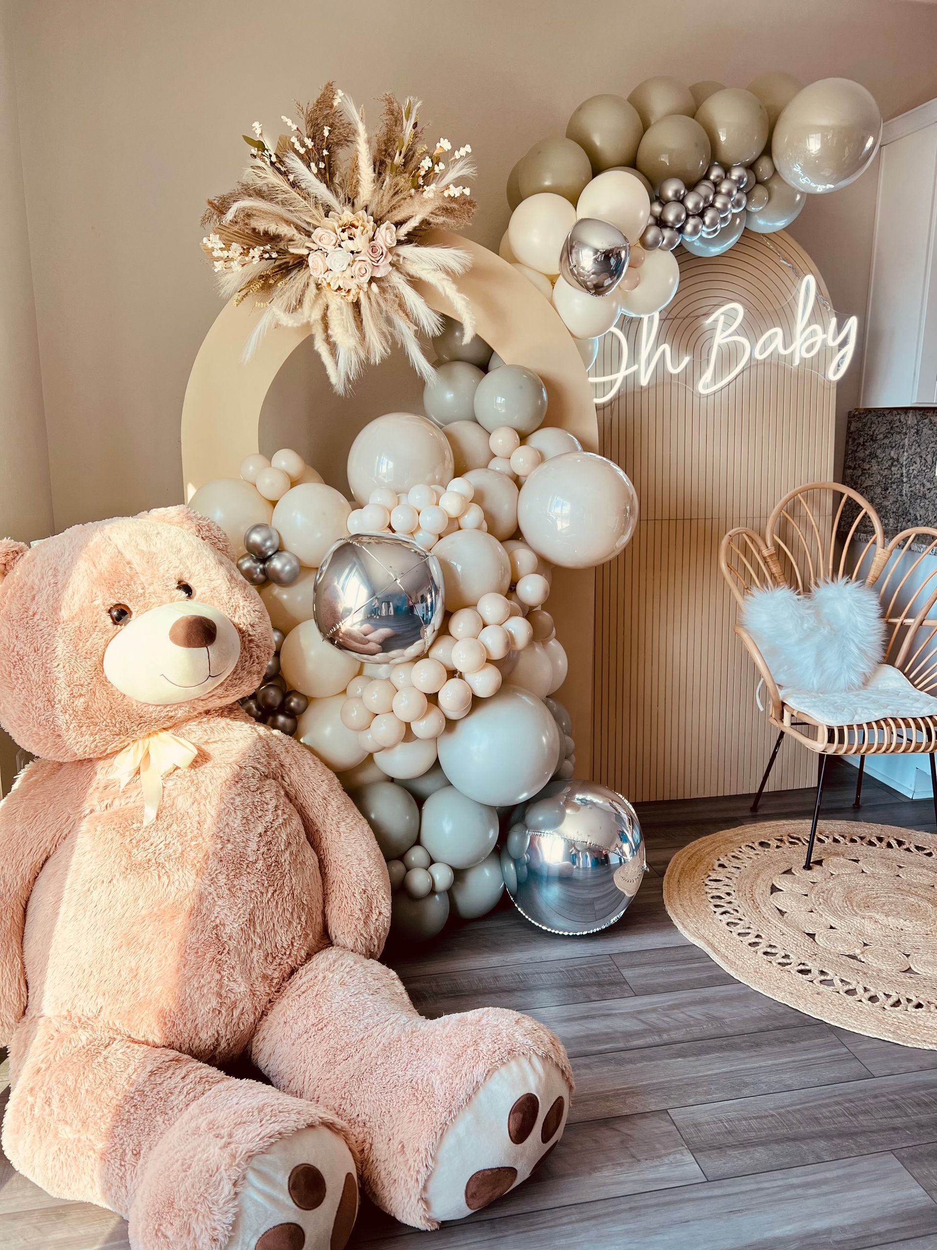 A teddy bear is sitting in front of a balloon arch.