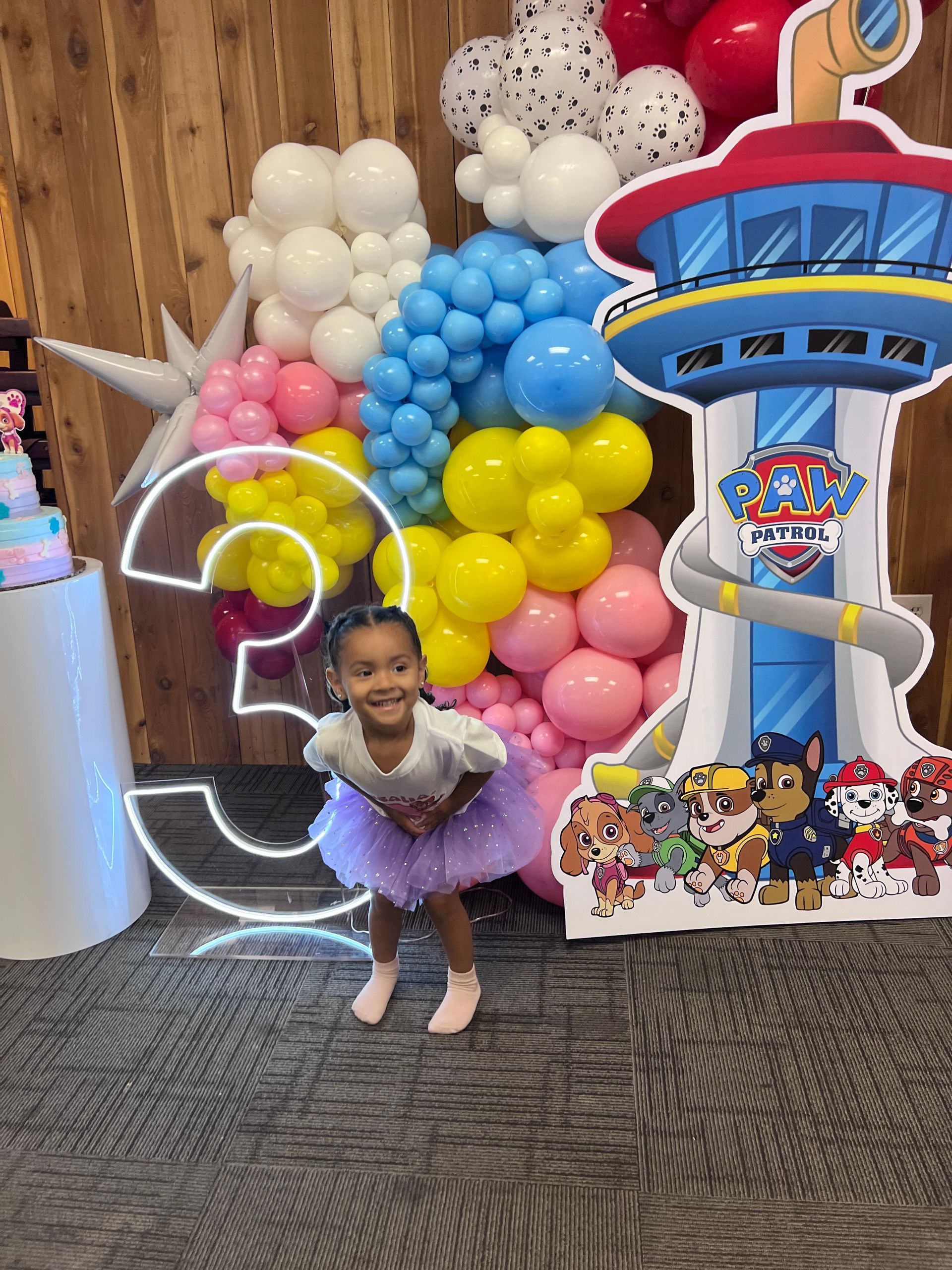A little girl is standing in front of a paw patrol sign.