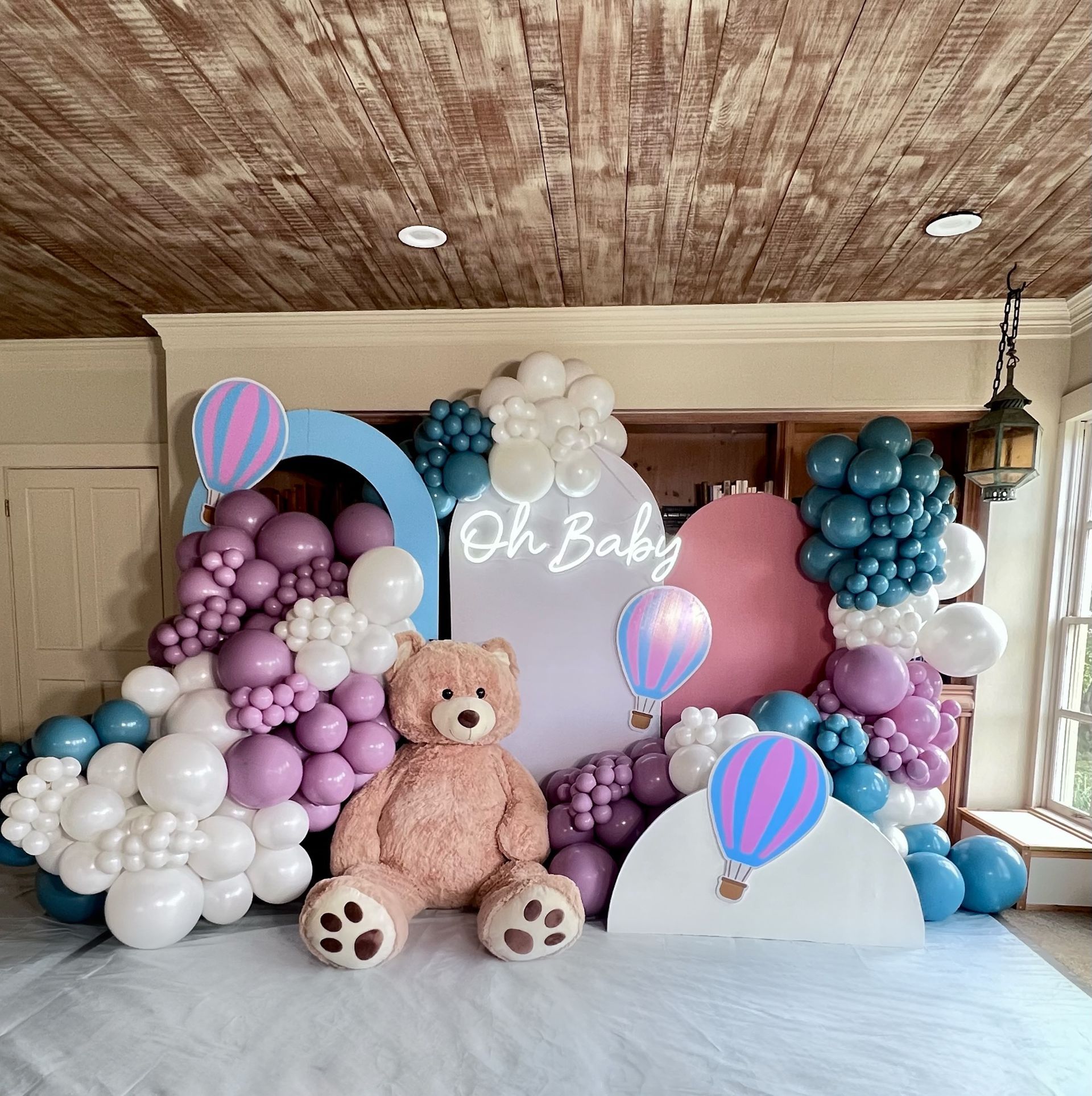 A teddy bear is sitting in front of a wall of balloons.