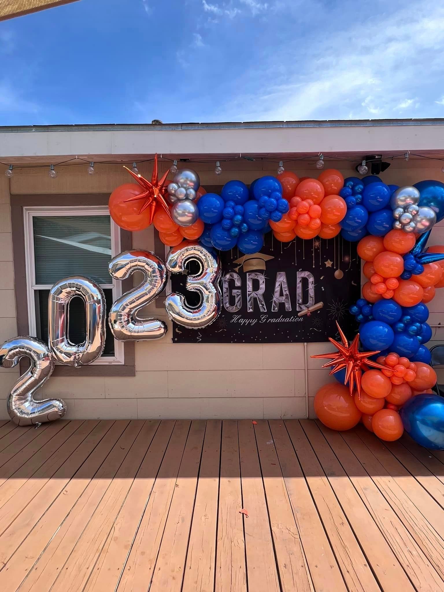 A bunch of balloons are sitting on a wooden deck in front of a house.