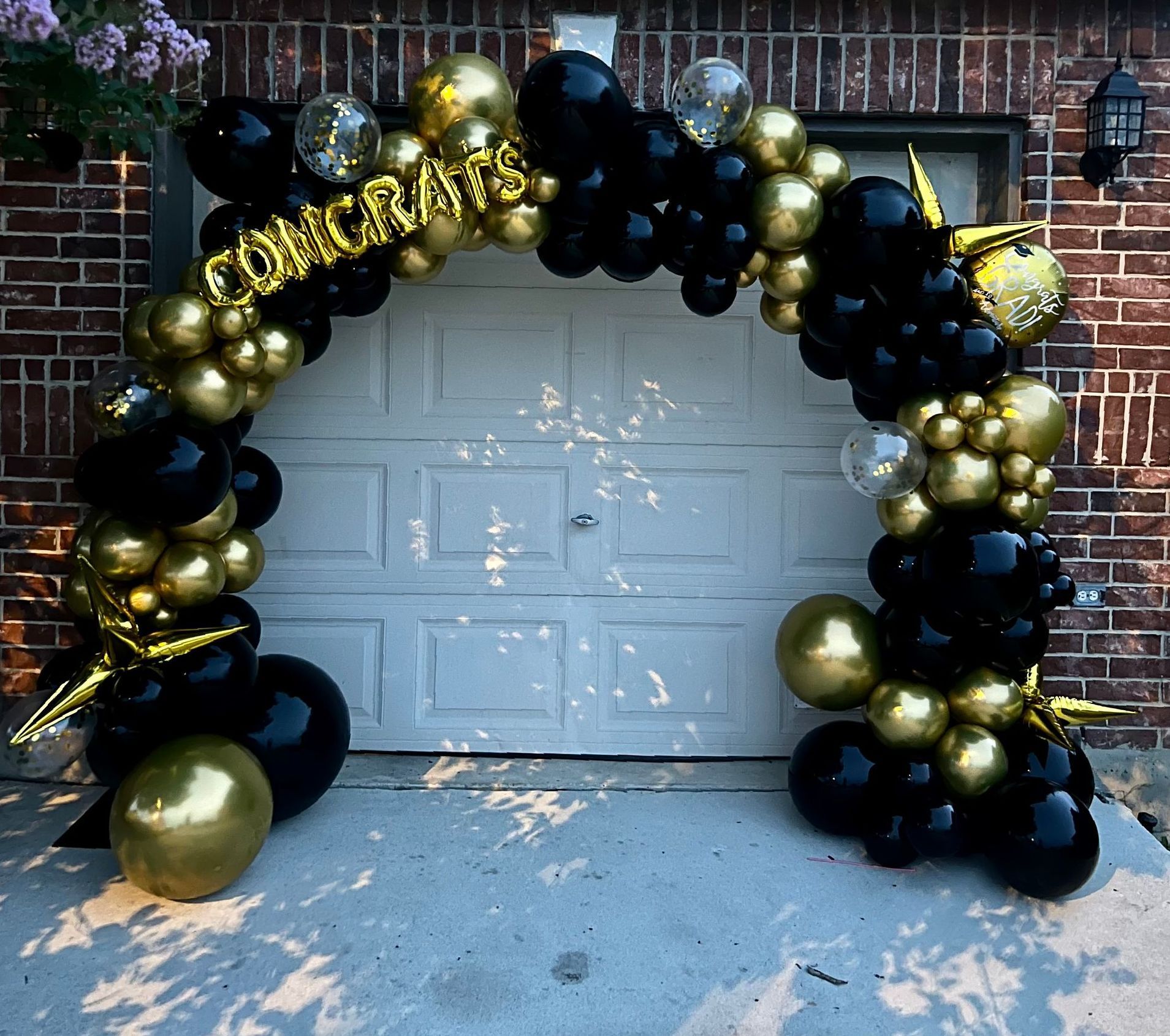 A black and gold balloon arch is in front of a garage door.