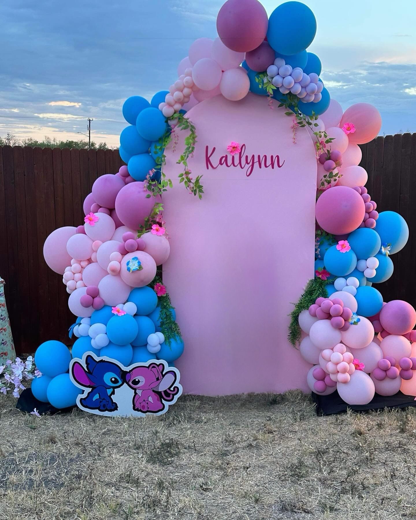 A pink wall decorated with pink and blue balloons and a stitch sign.