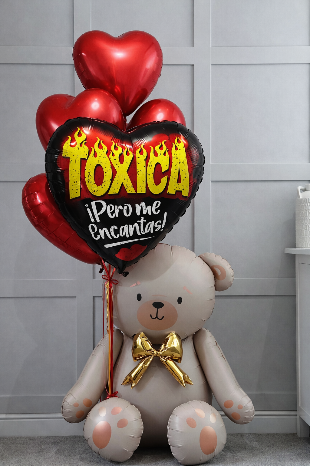 A light-colored teddy bear balloon holding a cluster of red heart balloons and a black heart balloon reading “Toxica.”