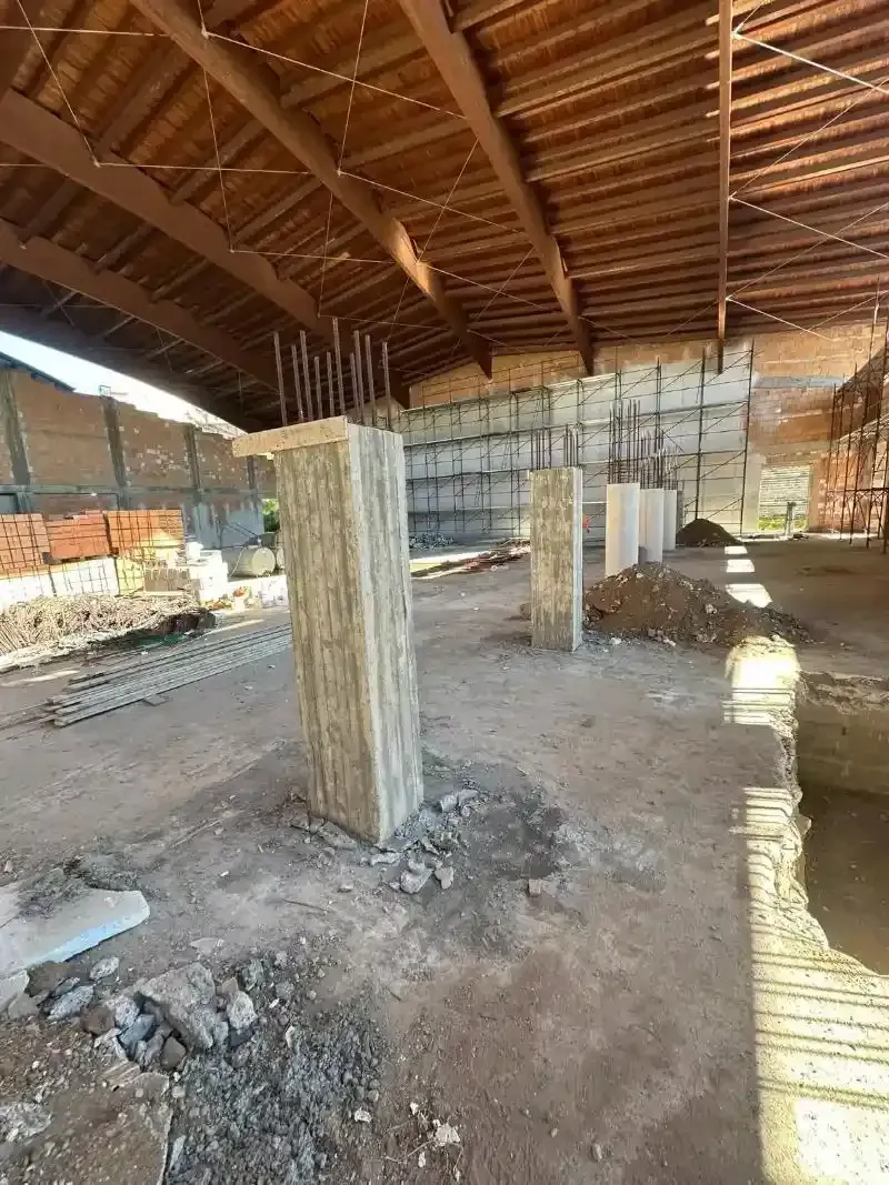 Vista interna di un edificio in costruzione, con pilastri in cemento, pareti in mattoni a vista e tetto in legno.