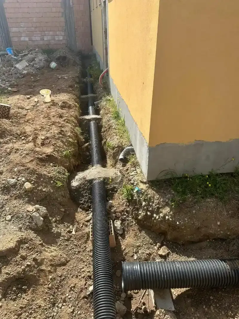 Tubi di drenaggio ondulati neri installati in una trincea accanto a un edificio giallo.