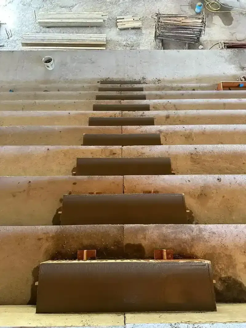 Gradini in cemento in costruzione, alcuni con pedate in materiale marrone. Legno e materiali da costruzione sullo sfondo.
