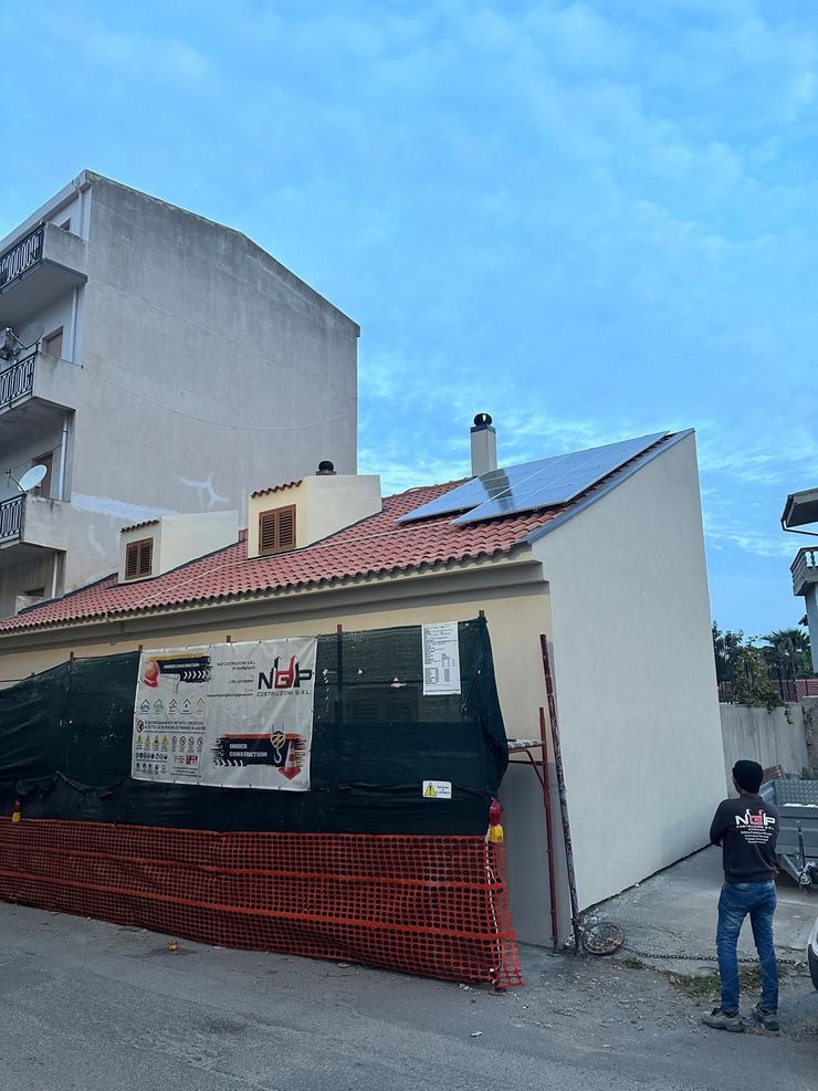 Edificio con impalcature, in fase di ristrutturazione. Facciata bianca, cielo azzurro e materiali da costruzione.