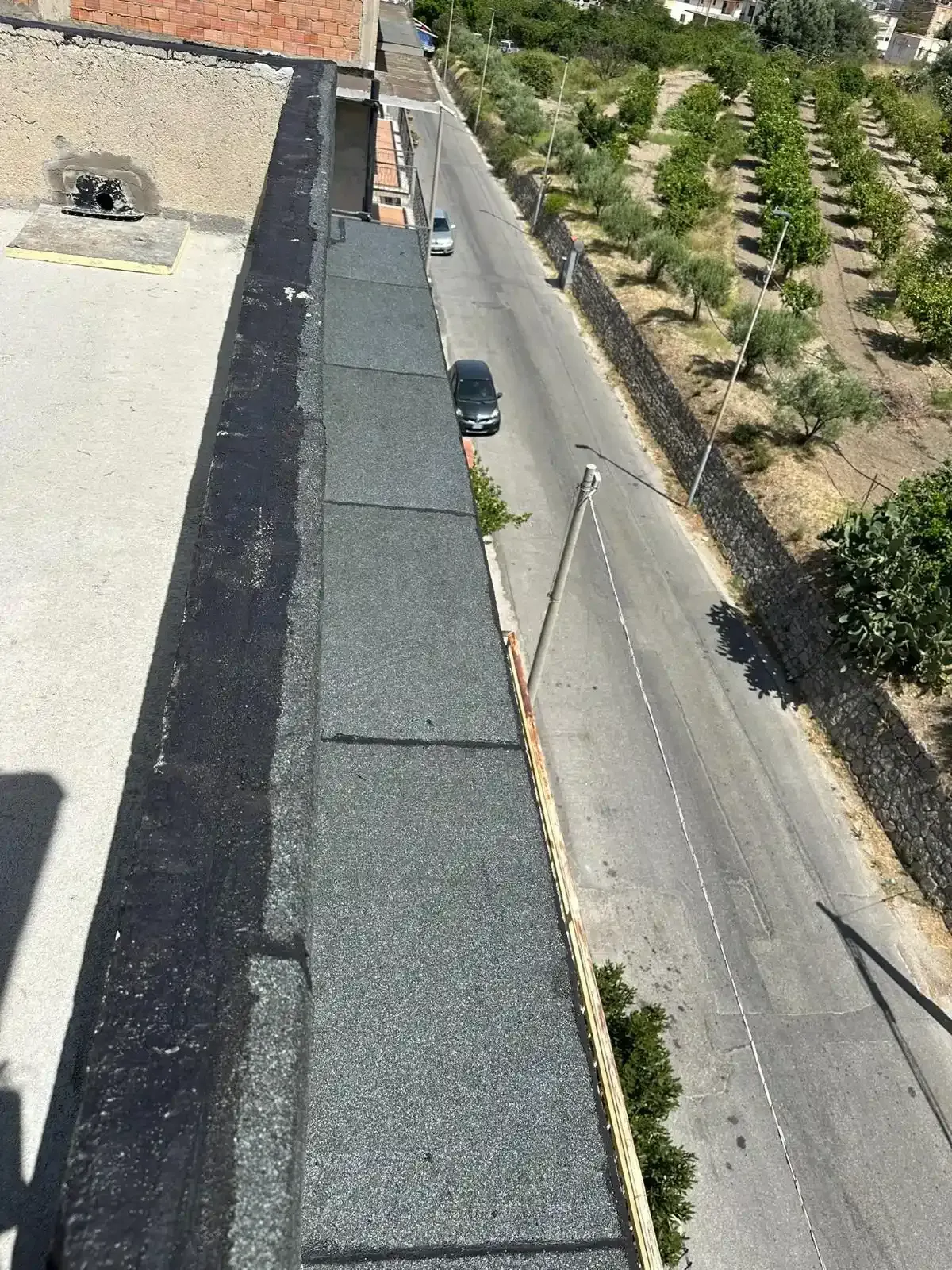 Vista da un tetto, che mostra un passaggio pedonale pavimentato e una strada con auto, fiancheggiata da alberi.