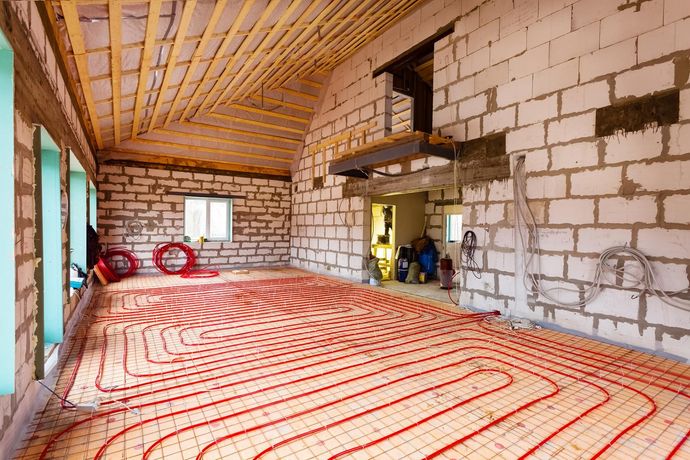 Vista interna della costruzione che mostra l'installazione del sistema di riscaldamento a pavimento radiante con tubi rossi, su una soletta di cemento.