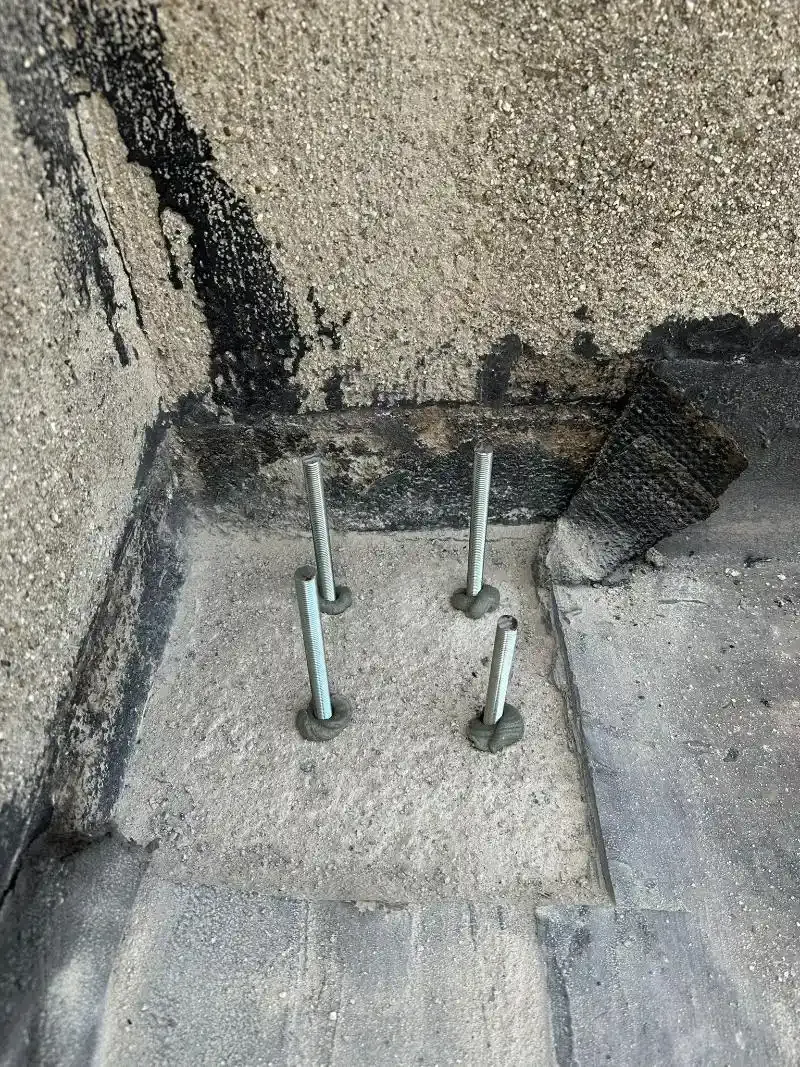 Quattro bulloni metallici con rondelle inseriti in una base di cemento, probabilmente per fissare attrezzature su un tetto.