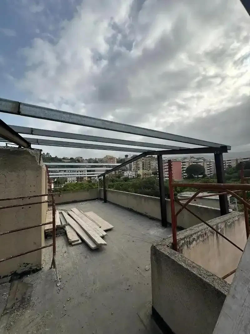 Tetto con struttura in metallo, pareti in cemento e cielo nuvoloso.