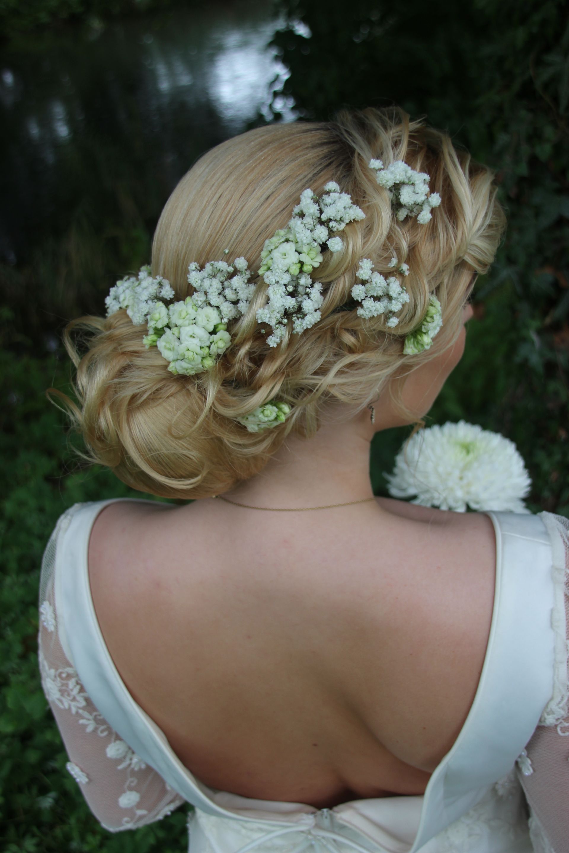 Kvinde set bagfra i en hvid kjole med en blomsterkrone og blomster i sin blonde frisure