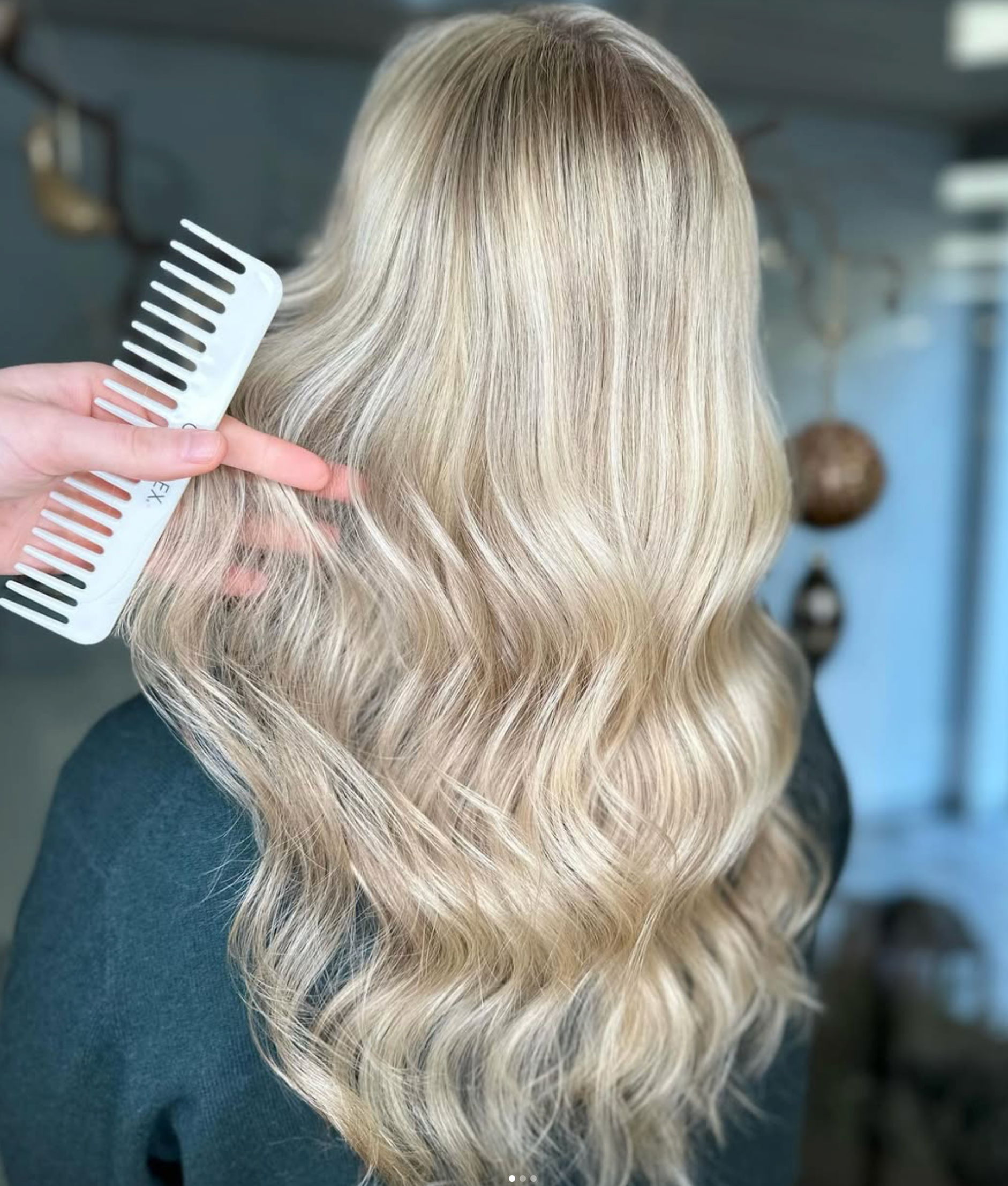 Blondt, bølget hår bliver redt med en bredtandet kam i en salon.
