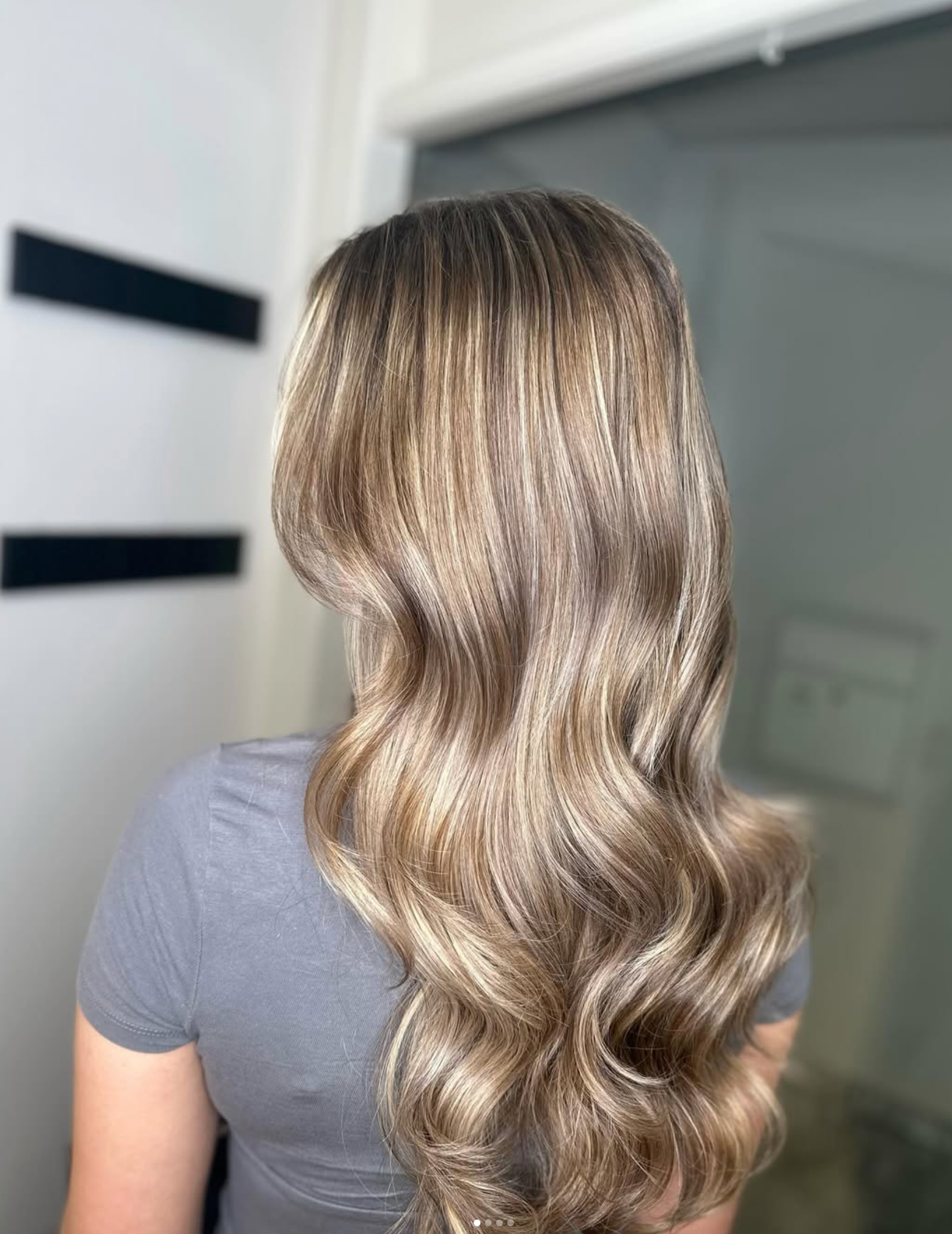 Langt bølget brunt hår med blonde striber, vist bagfra i en salon.