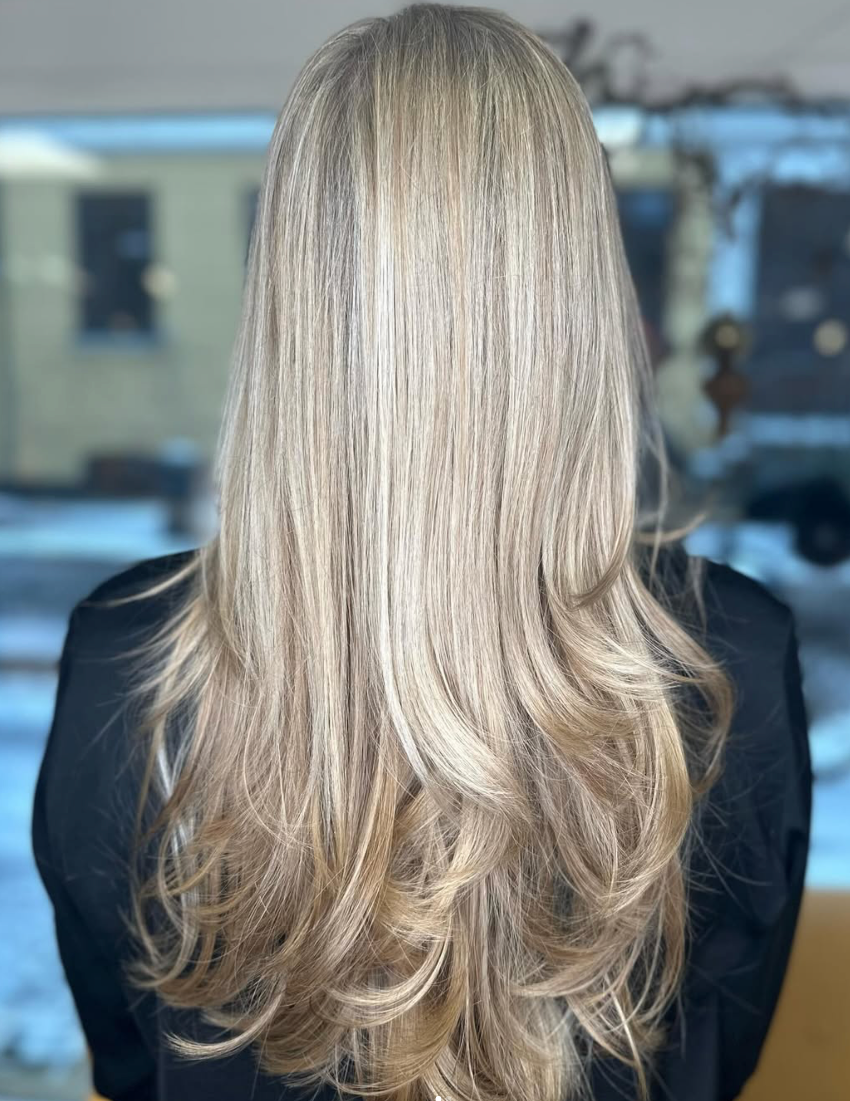 Langt blondt hår i lag med bløde bølger, set bagfra i en salon