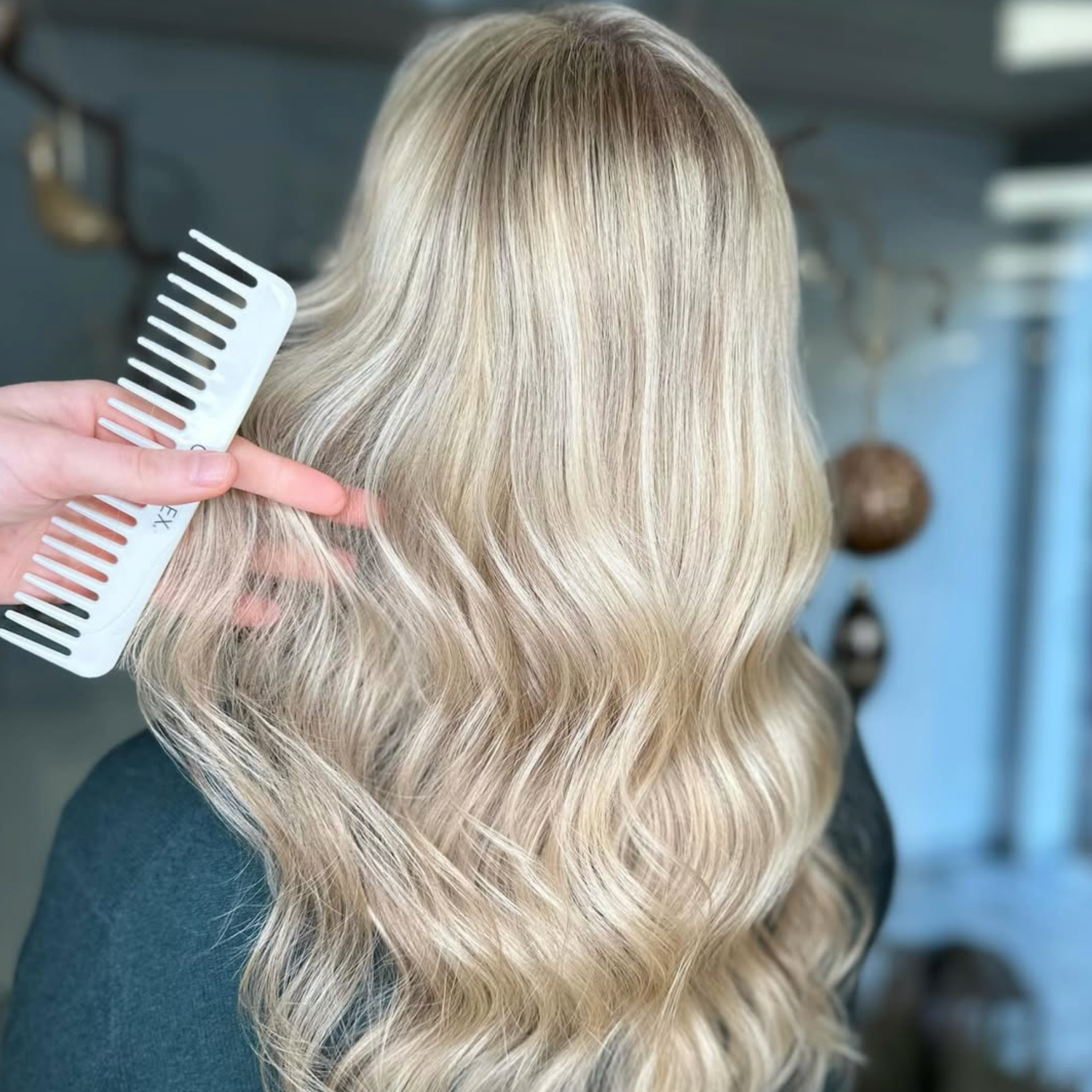 Blondt, bølget hår, der bliver redt, vist bagfra i en salon