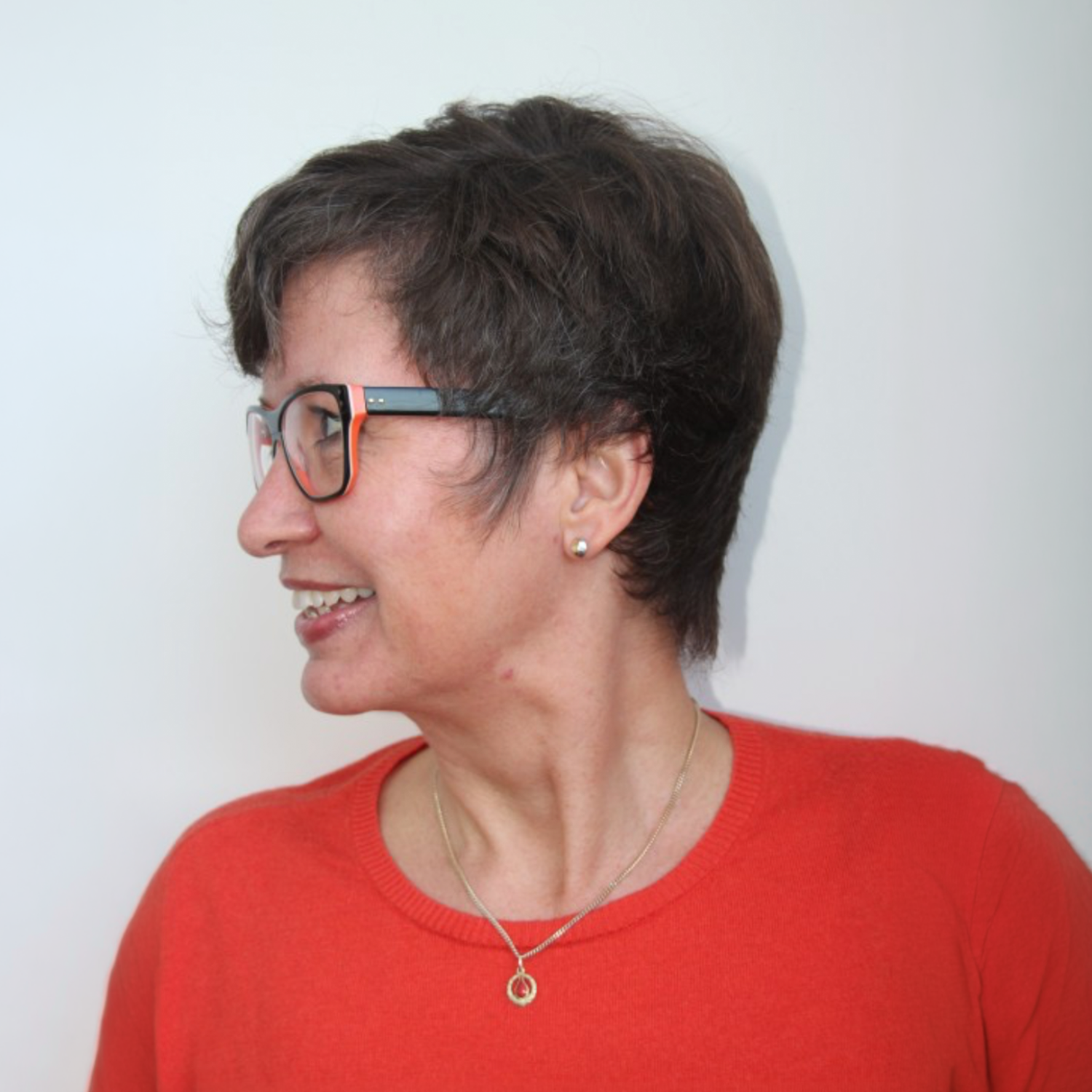 Profil af en smilende person med kort mørkt hår, briller og en rød top mod en lys baggrund