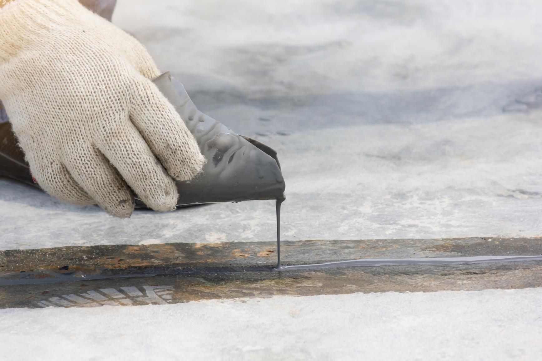 Gloved Hand Applying Black Sealant to a Concrete Joint Outdoors — Australian Epoxy Floors in Rockhampton, QLD