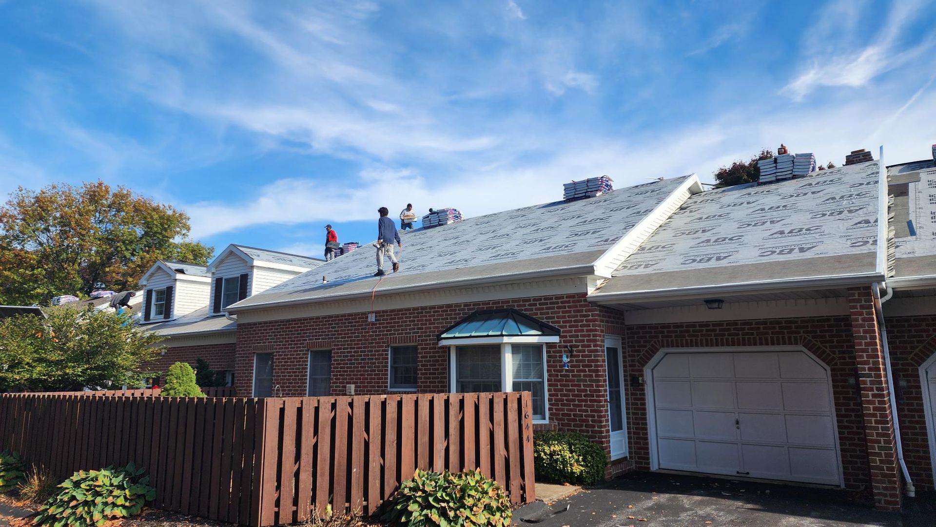 A group of people are working on the roof of a brick house.