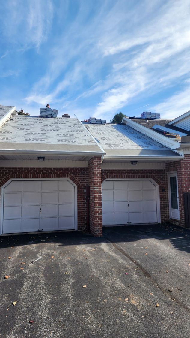 A brick house with two white garage doors and a blue sky in the background.