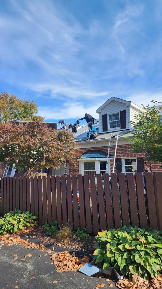 A man is working on the roof of a house next to a wooden fence.