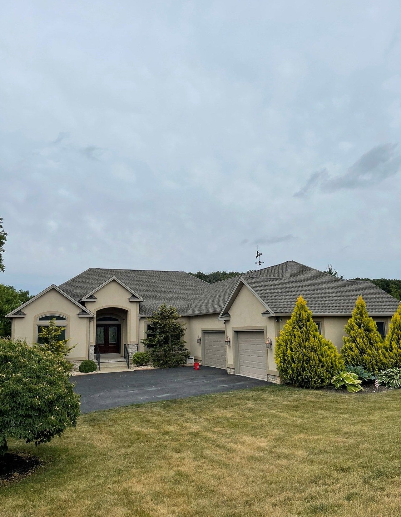 Suburban house with gray roof, driveway, and manicured lawn under cloudy sky Suburban house with gray roof, driveway, and manicured lawn under cloudy sky
