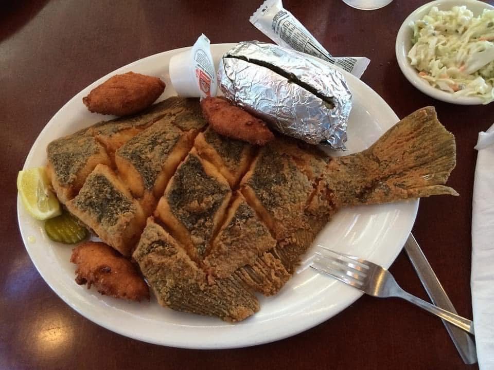 Plate of fried fish with lemon wedges, a baked potato, and coleslaw on a restaurant table