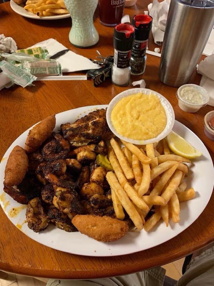 Plate of barbecue chicken, fries, and mac and cheese on a wooden table with drinks in the background